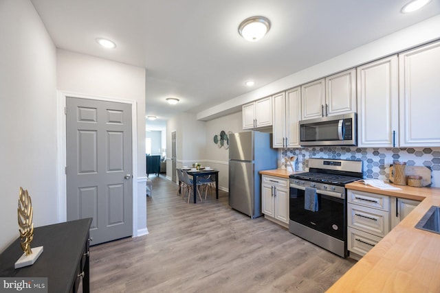 kitchen featuring light wood-type flooring, backsplash, appliances with stainless steel finishes, and wooden counters