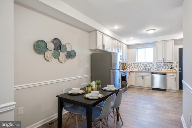 kitchen with appliances with stainless steel finishes, light wood-type flooring, white cabinetry, and backsplash