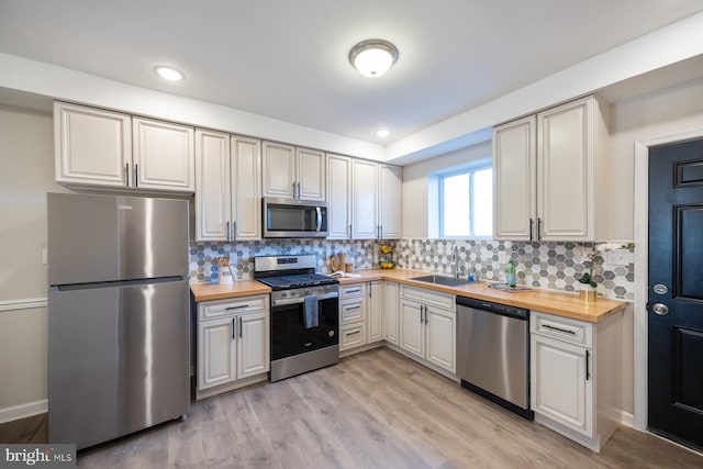 kitchen with wood counters, tasteful backsplash, stainless steel appliances, sink, and light hardwood / wood-style flooring