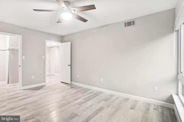 unfurnished bedroom with ceiling fan, a walk in closet, light wood-type flooring, and a closet