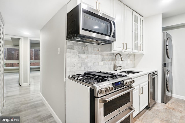 kitchen featuring white cabinets, stacked washer / drying machine, sink, and appliances with stainless steel finishes