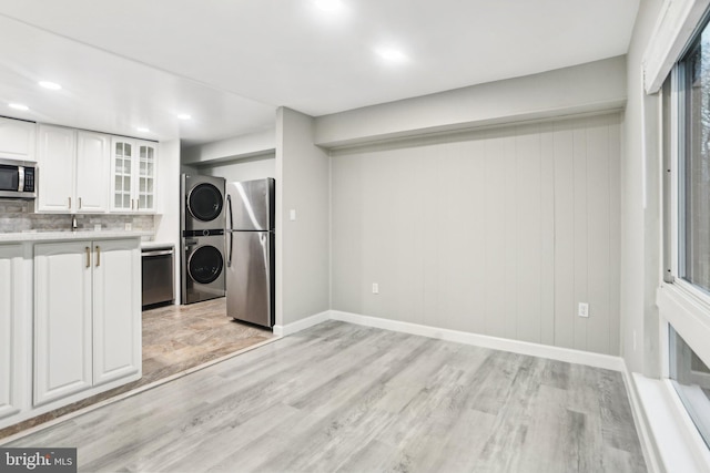 kitchen with backsplash, stacked washer / dryer, appliances with stainless steel finishes, white cabinets, and light wood-type flooring