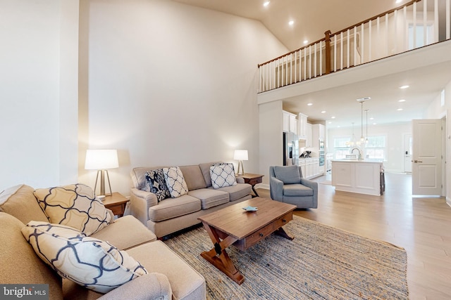 living room with a towering ceiling, sink, and light hardwood / wood-style flooring