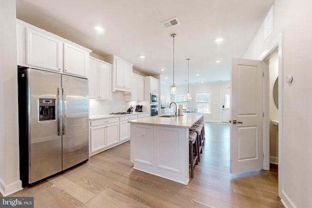 kitchen with sink, hanging light fixtures, an island with sink, white cabinets, and appliances with stainless steel finishes