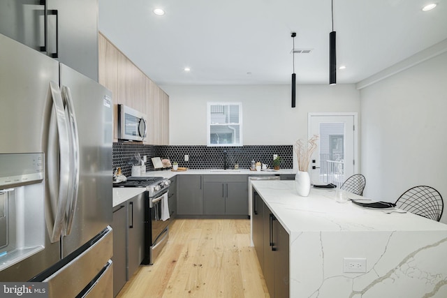 kitchen with backsplash, gray cabinetry, stainless steel appliances, light hardwood / wood-style floors, and hanging light fixtures