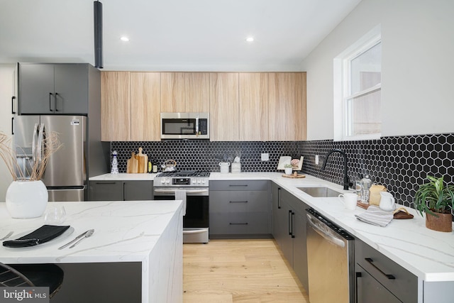 kitchen with sink, gray cabinets, light wood-type flooring, appliances with stainless steel finishes, and light stone counters