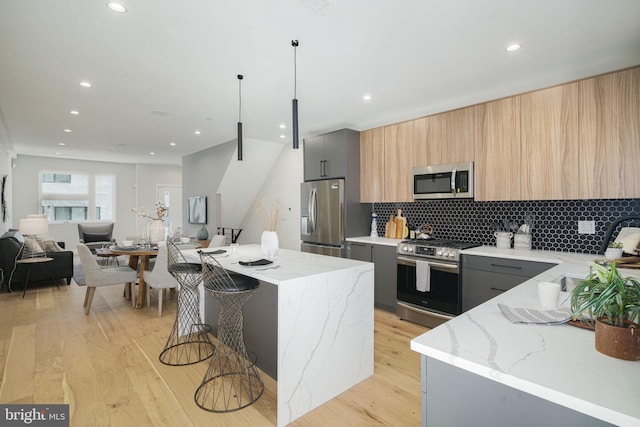 kitchen with gray cabinetry, light stone countertops, a center island, a kitchen breakfast bar, and appliances with stainless steel finishes