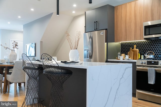 kitchen with a center island, light stone counters, light wood-type flooring, and appliances with stainless steel finishes