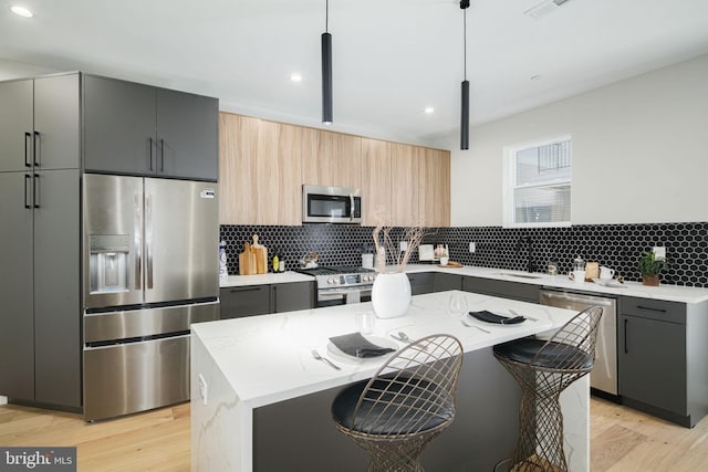 kitchen with light stone countertops, appliances with stainless steel finishes, decorative light fixtures, a center island, and light hardwood / wood-style floors