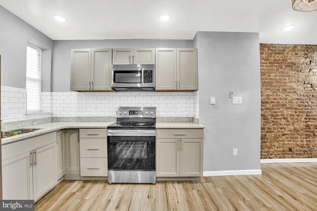 kitchen featuring backsplash, gray cabinets, light stone countertops, light wood-type flooring, and appliances with stainless steel finishes