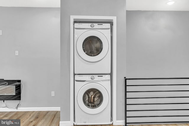 laundry room with stacked washing maching and dryer and light hardwood / wood-style floors