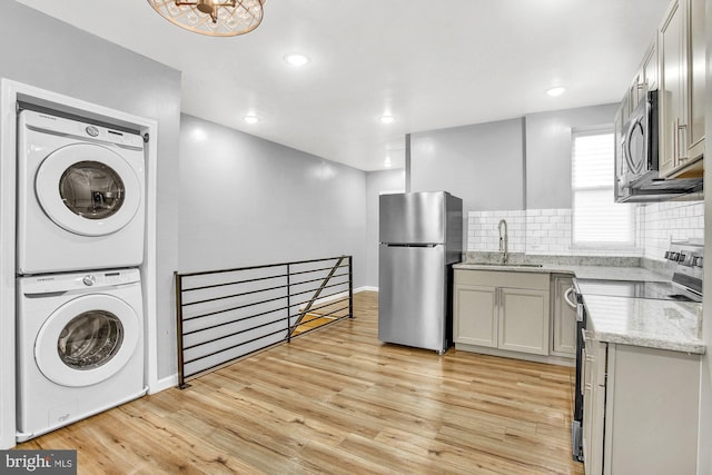 kitchen featuring sink, light wood-type flooring, stacked washer / drying machine, and appliances with stainless steel finishes