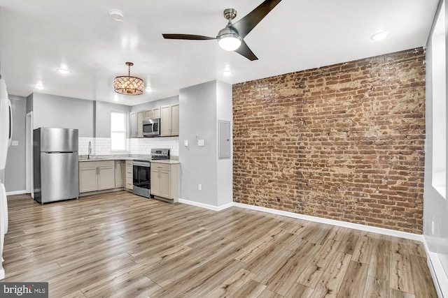 kitchen with light wood-type flooring, brick wall, stainless steel appliances, ceiling fan, and sink