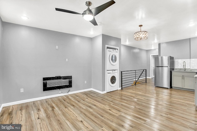 unfurnished living room featuring sink, stacked washing maching and dryer, heating unit, light hardwood / wood-style floors, and ceiling fan with notable chandelier