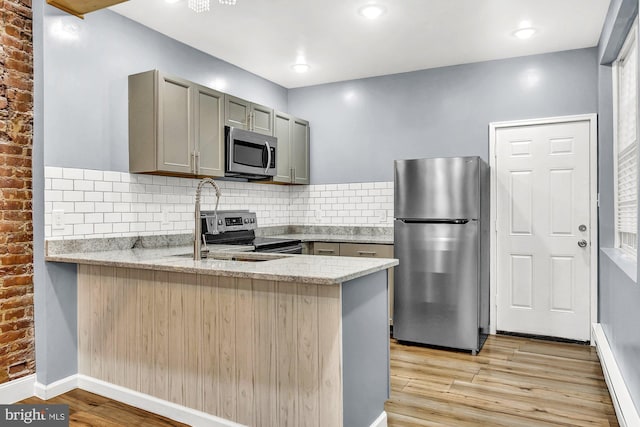 kitchen featuring kitchen peninsula, light wood-type flooring, backsplash, brick wall, and stainless steel appliances