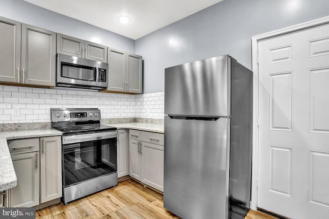 kitchen with decorative backsplash, stainless steel appliances, light hardwood / wood-style floors, and gray cabinetry