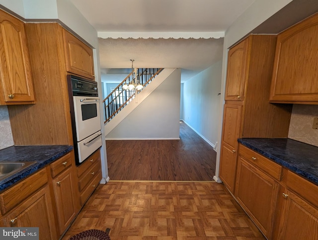 kitchen featuring decorative backsplash, parquet floors, white oven, a notable chandelier, and hanging light fixtures