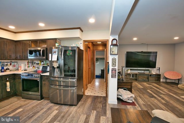 kitchen with appliances with stainless steel finishes, dark brown cabinetry, hardwood / wood-style flooring, and crown molding