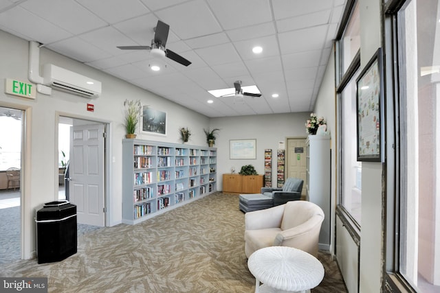 sitting room with ceiling fan, a drop ceiling, carpet floors, and a wall mounted air conditioner