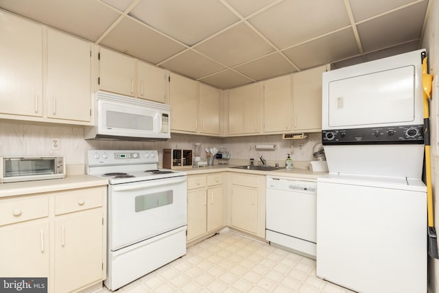 kitchen featuring a drop ceiling, sink, stacked washer and dryer, white appliances, and cream cabinetry