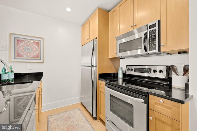 kitchen with a sink, baseboards, appliances with stainless steel finishes, and light brown cabinets