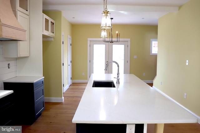 kitchen with tasteful backsplash, white cabinetry, sink, and a center island with sink