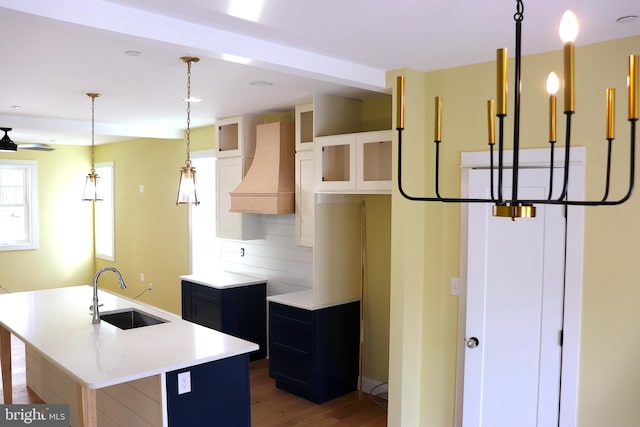 kitchen featuring sink, tasteful backsplash, hanging light fixtures, an island with sink, and white cabinets