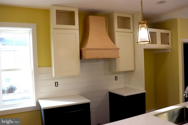 kitchen with white cabinetry, hanging light fixtures, sink, and premium range hood