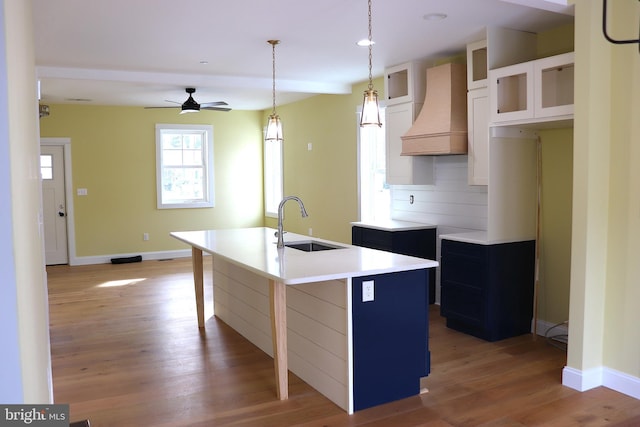 kitchen with sink, hanging light fixtures, custom range hood, a center island with sink, and decorative backsplash