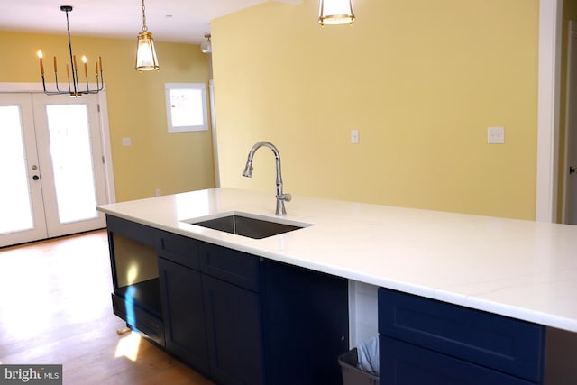 kitchen with light stone counters, sink, hanging light fixtures, and light wood-type flooring