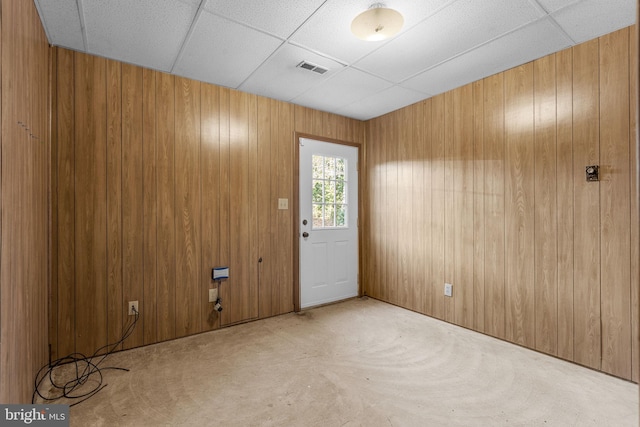 unfurnished room with light carpet, a paneled ceiling, and wood walls