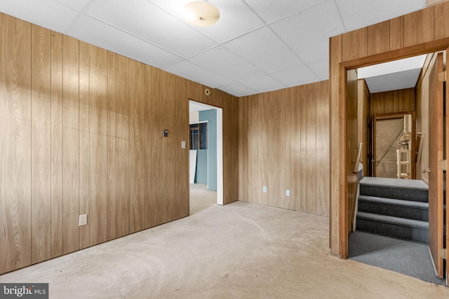 carpeted spare room with a paneled ceiling and wooden walls