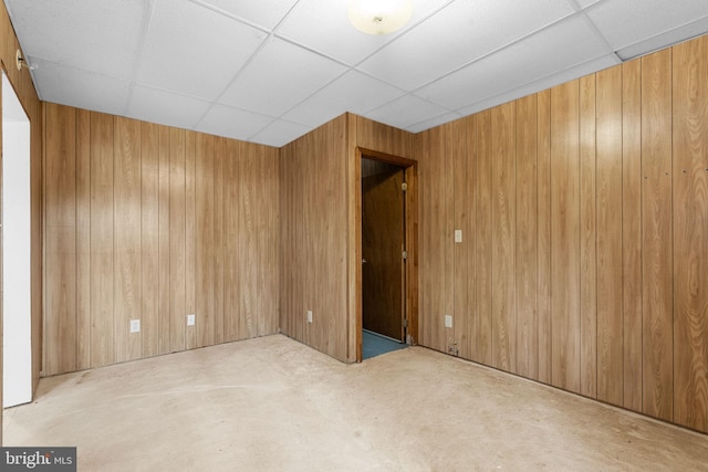 unfurnished room with wooden walls and a drop ceiling