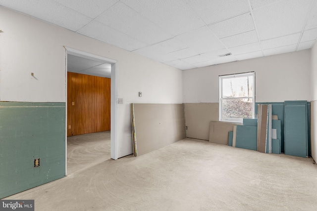 carpeted spare room featuring wood walls and a drop ceiling