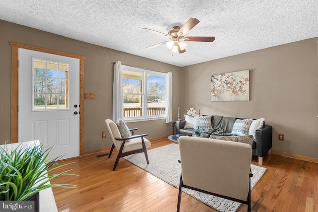 living room featuring ceiling fan, light wood-type flooring, and a textured ceiling