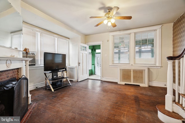 living room with radiator heating unit, dark wood-type flooring, a brick fireplace, and ceiling fan