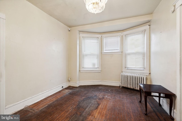 spare room featuring radiator heating unit, dark hardwood / wood-style flooring, and a chandelier