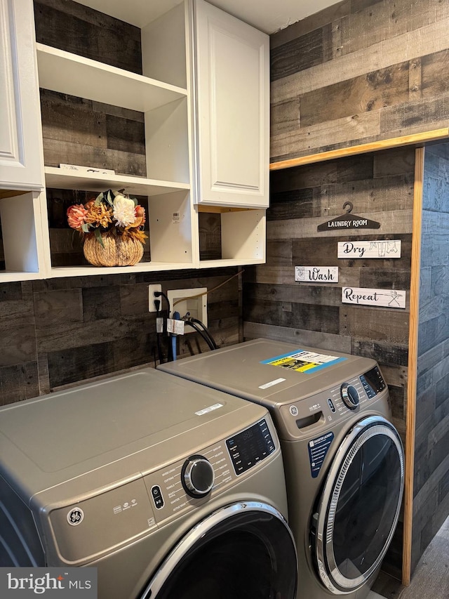 laundry area featuring washing machine and clothes dryer, wooden walls, and cabinets