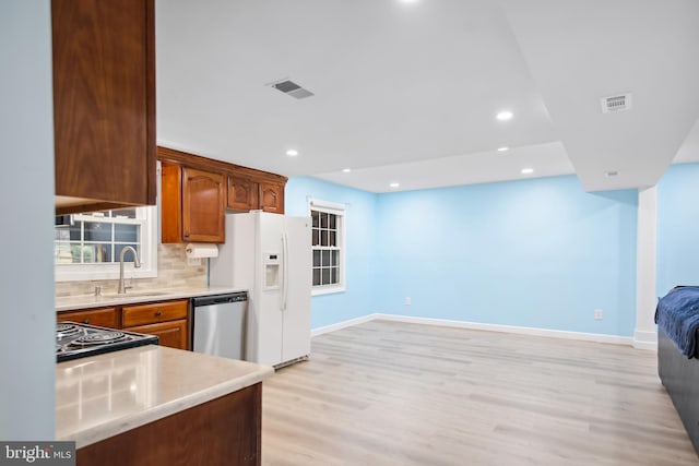 kitchen with appliances with stainless steel finishes, backsplash, light hardwood / wood-style floors, and sink