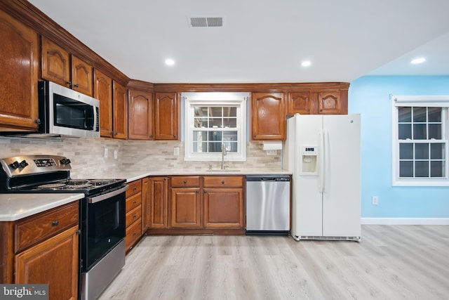 kitchen with tasteful backsplash, sink, stainless steel appliances, and light hardwood / wood-style floors