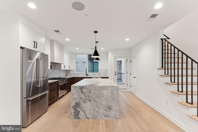 kitchen featuring white cabinetry, wall chimney exhaust hood, hanging light fixtures, premium appliances, and light hardwood / wood-style flooring