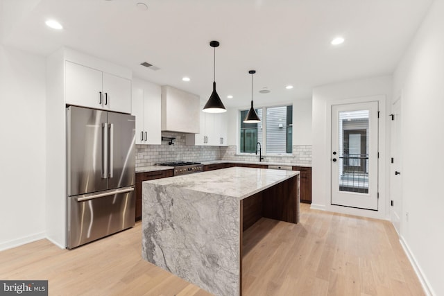 kitchen featuring a center island, light stone counters, appliances with stainless steel finishes, white cabinets, and light wood-type flooring