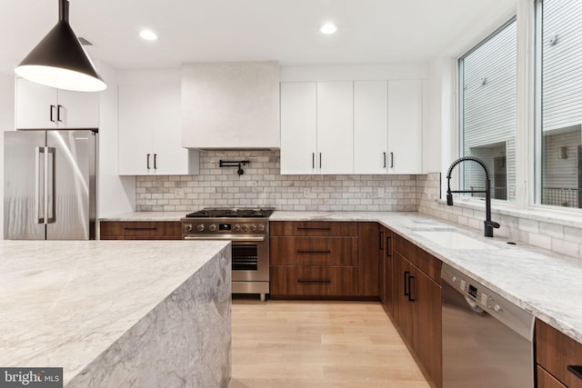 kitchen featuring custom exhaust hood, light hardwood / wood-style flooring, appliances with stainless steel finishes, decorative light fixtures, and white cabinetry