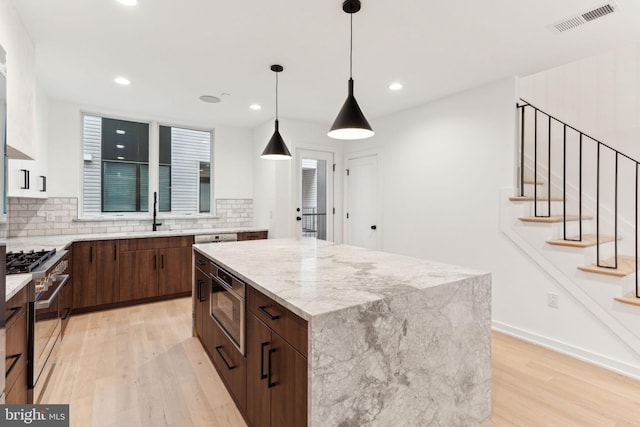 kitchen featuring a center island, stainless steel appliances, hanging light fixtures, and light hardwood / wood-style floors