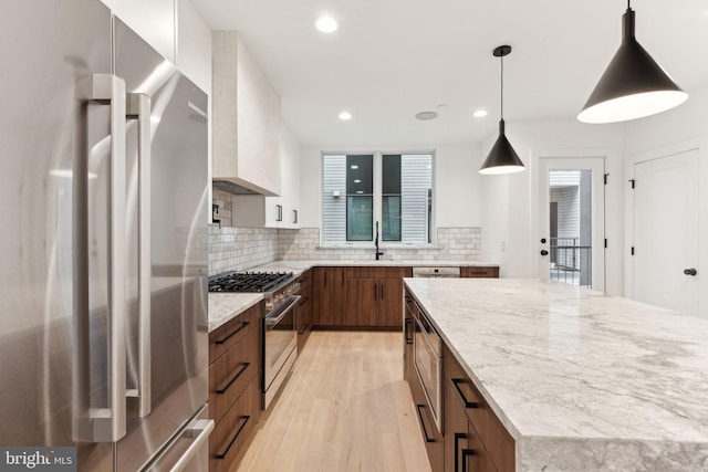 kitchen with sink, hanging light fixtures, light hardwood / wood-style floors, high quality appliances, and custom range hood