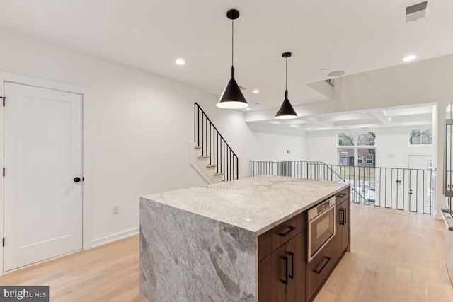 kitchen featuring light stone countertops, stainless steel microwave, light hardwood / wood-style flooring, a center island, and hanging light fixtures