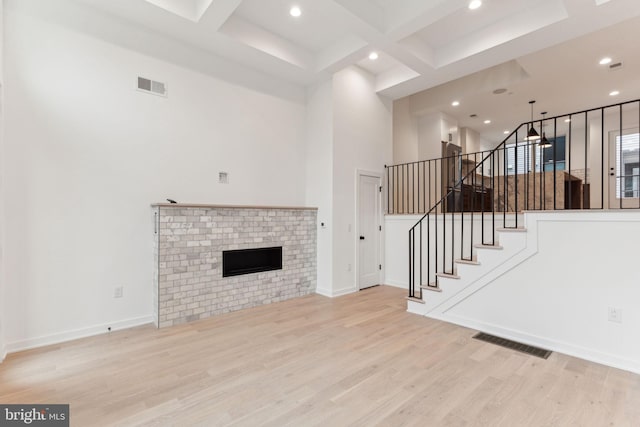 unfurnished living room with a high ceiling, coffered ceiling, a brick fireplace, beamed ceiling, and light hardwood / wood-style floors