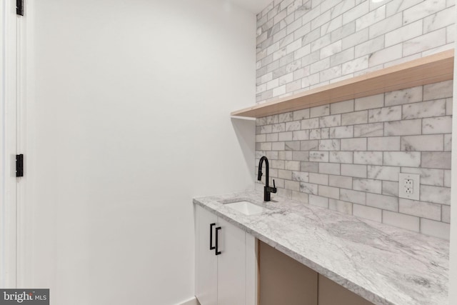 bar featuring light stone countertops, sink, and tasteful backsplash