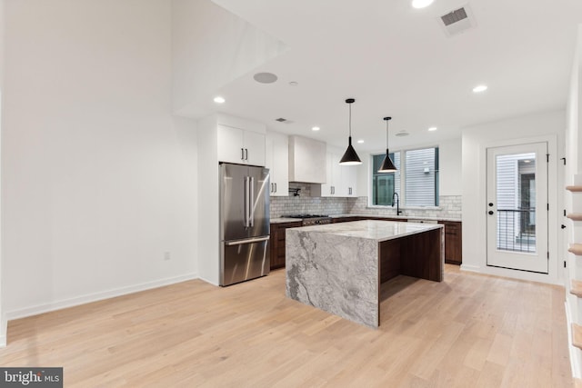 kitchen with a center island, hanging light fixtures, light hardwood / wood-style flooring, high end fridge, and dark brown cabinetry