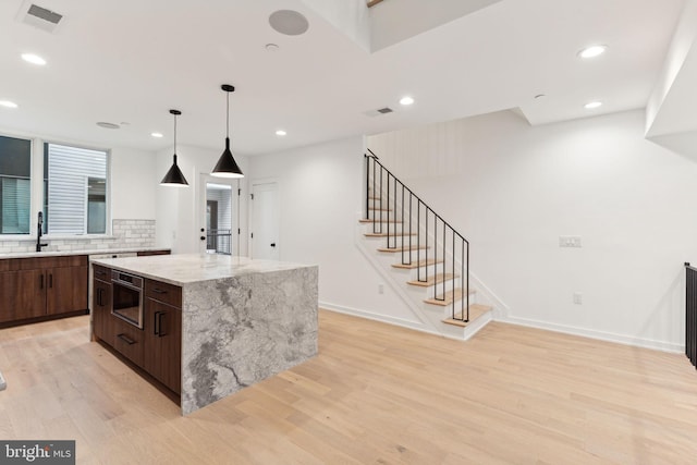 kitchen with sink, light hardwood / wood-style flooring, dark brown cabinets, a kitchen island, and light stone counters